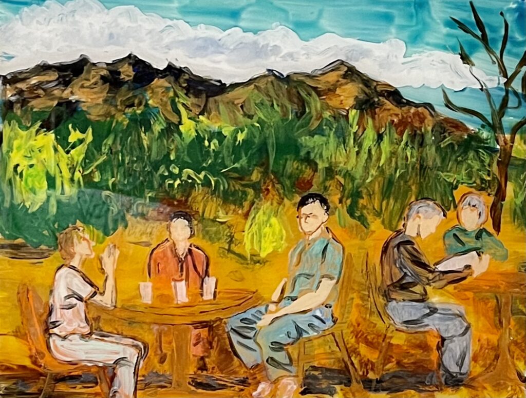 A scene in the Western part of America, with mountains in the the background. In the foreground on the left, three figures sitting at a table - two women and a man; on the right, two figures at another table, the man reading.